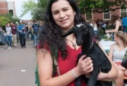 A female student on on a busy campus holding a baby goat