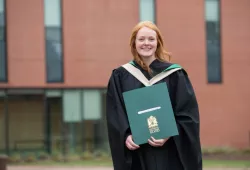 Photo of female graduate holding her degree on the UPEI campus