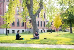 two students sitting in the UPEI quad with a large brick building in the background