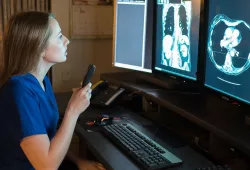a radiographer reviewing two images on two computer screens