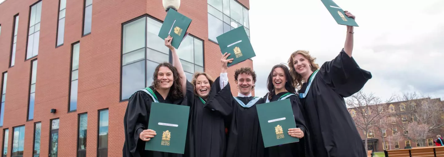 a group of five UPEI graduates holding degrees in front of the Health Sciences Building