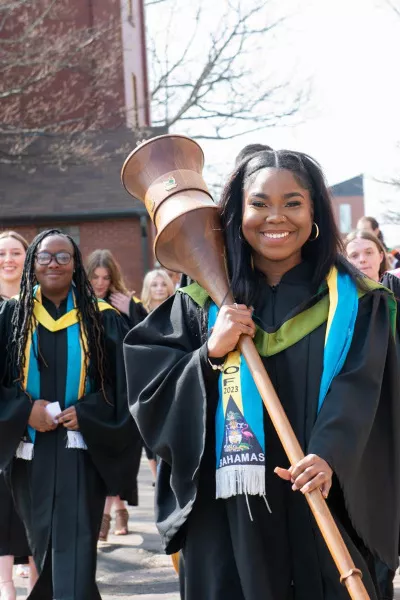 a smiling UPEI graduate holding the ceremonial mace leading a procession of other graduates