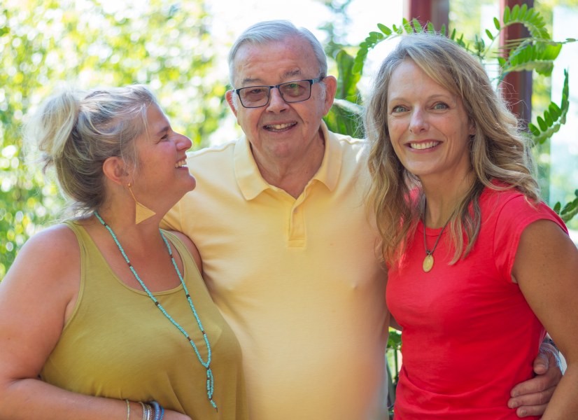 Two smiling women flank a smiling older man no a sunny day. All look happy and relaxed.