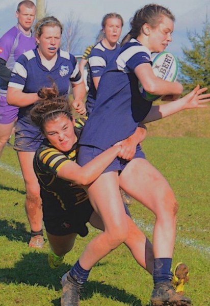 Picture of woman rugby player tackling another who is carrying ball with teammates looking on