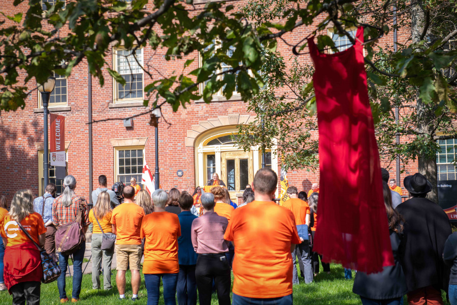 Photo of people standing in the quad listening to a speaker and wearing orange for National Day for Truth and Reconciliation watching 