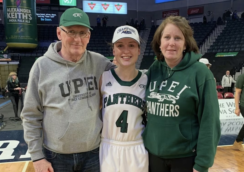 photo of man and woman standing on either side of basketball player, all wearing UPEI branded clothing
