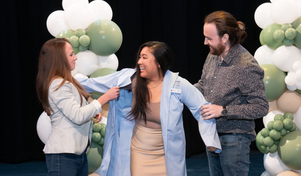 Giselle Kan, Class of 2028, receives her blue coat from her partner, Austin Gautreau, and her mentor and AVC alumna Dr. Lauren Brooks. 