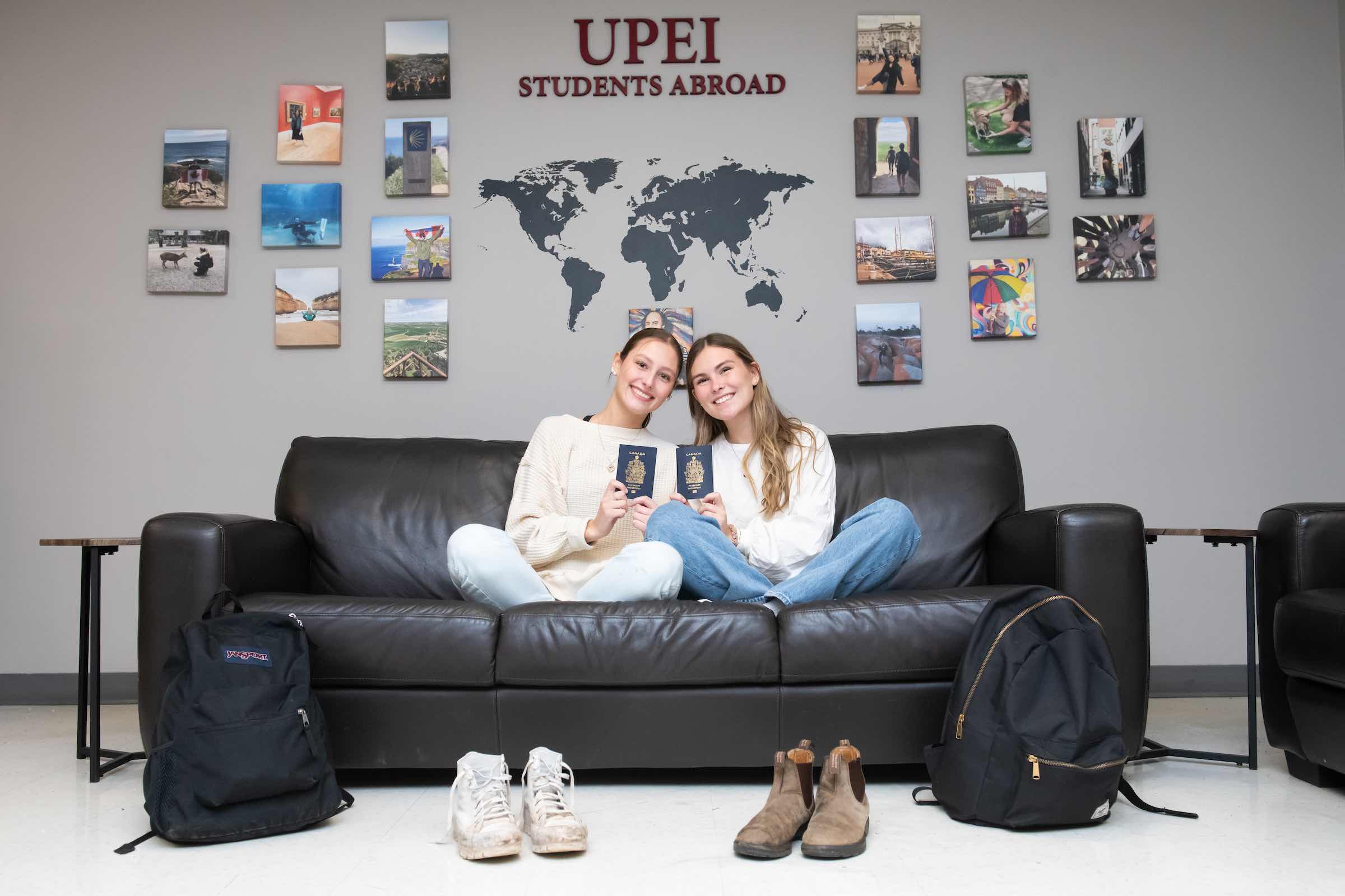 two students holding passports in front of photos of other countries