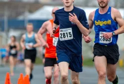 A young man running in a road race looking strong and confident with other runners trailing him