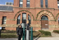 UPEI Environmental Studies student Ajhma Dhakal stands outside Charlottetown City Hall next to one of the city’s Electric Vehicle (EV) chargers