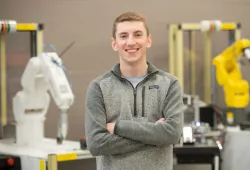 photo of young man standing with arms folded in front of engineering lab equipment