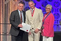 Photo of two people presenting a man with a certificate and medal