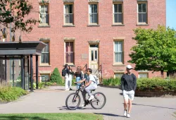 photo of person biking and others walking on a brick pathway on campus