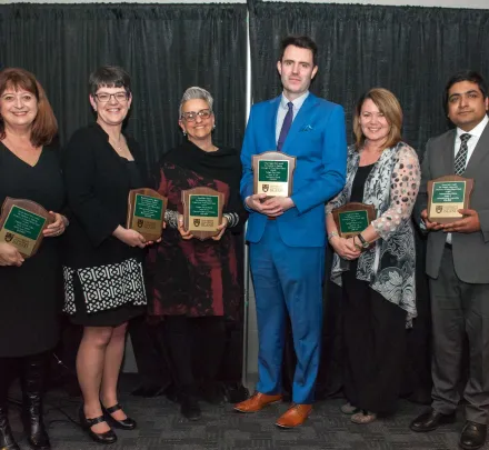 six award winning professors holding award plaques