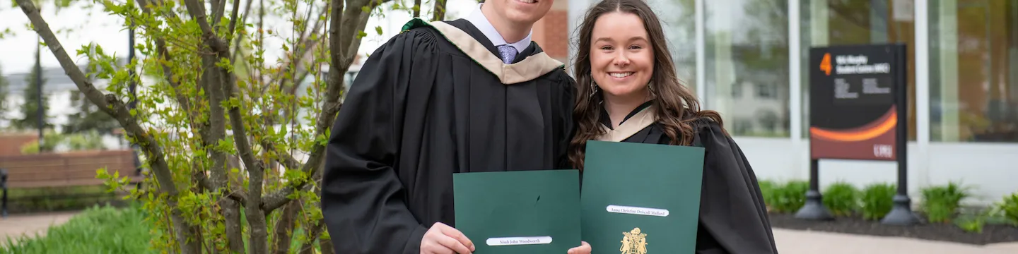 two UPEI graduates holding their degrees