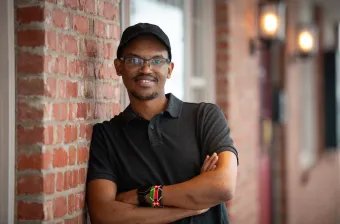 a smiling man standing by a brick wall