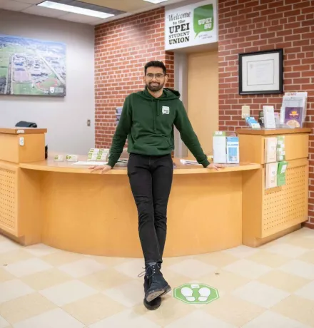 a UPEI student in a green UPEISU hoodie standing in an office