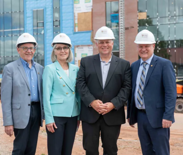Photo of four people wearing hard hats standing in front of a building under construction