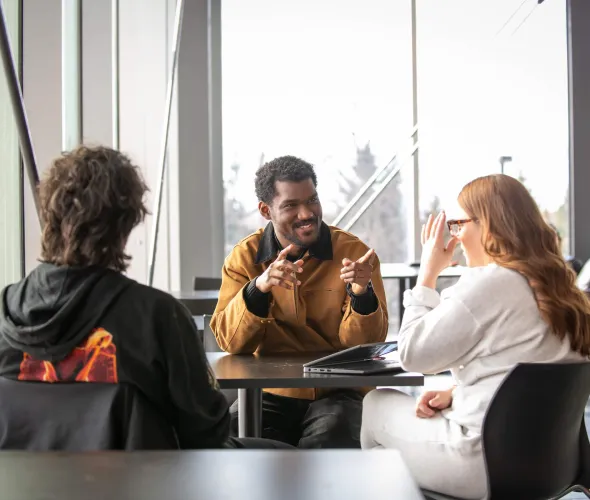 three students talking at a small table